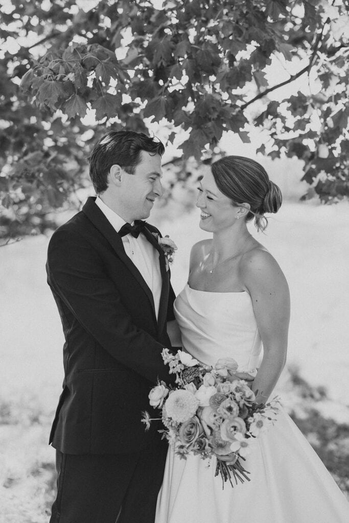 Black and white film portrait of Jena and James laughing together under a tree at the Philadelphia Cricket Club, a Chestnut Hill Philadelphia wedding