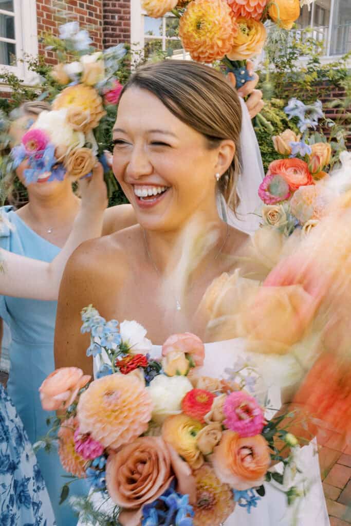 Jena laughing as her bridesmaids in blue lift their colorful bouquets around her, the bridal flowers blurring in motion, candid Philadelphia Cricket Club wedding photos