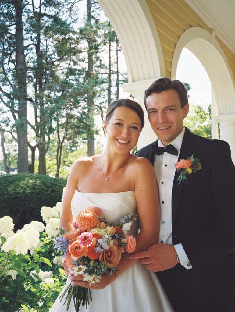 Film portrait of Jena and James smiling together beneath the yellow arched porch and white hydrangeas, a favorite from their Philadelphia Cricket Club wedding photos in September