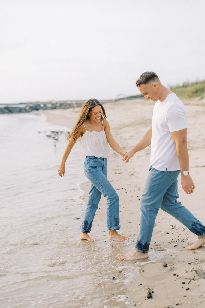 Carolyn and Zach walking barefoot through the shallow surf holding hands at their Cape May beach engagement session