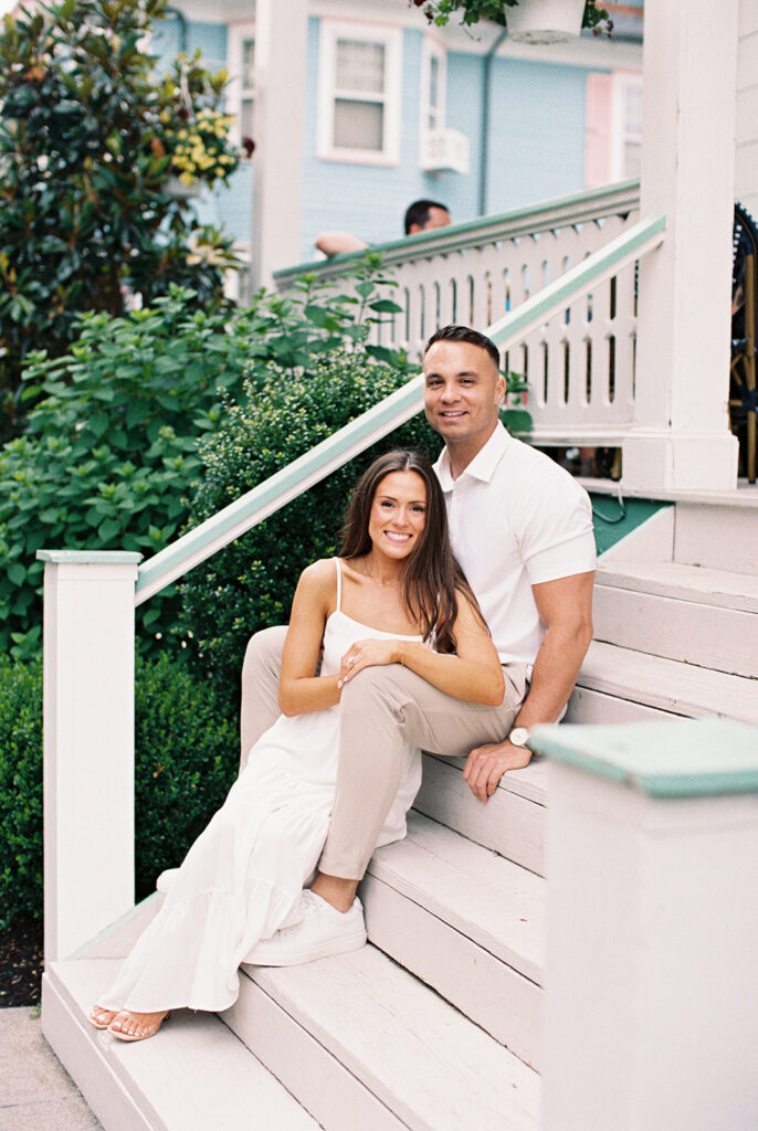 Carolyn and Zach seated on the steps of a pastel Victorian home in Cape May during their engagement session