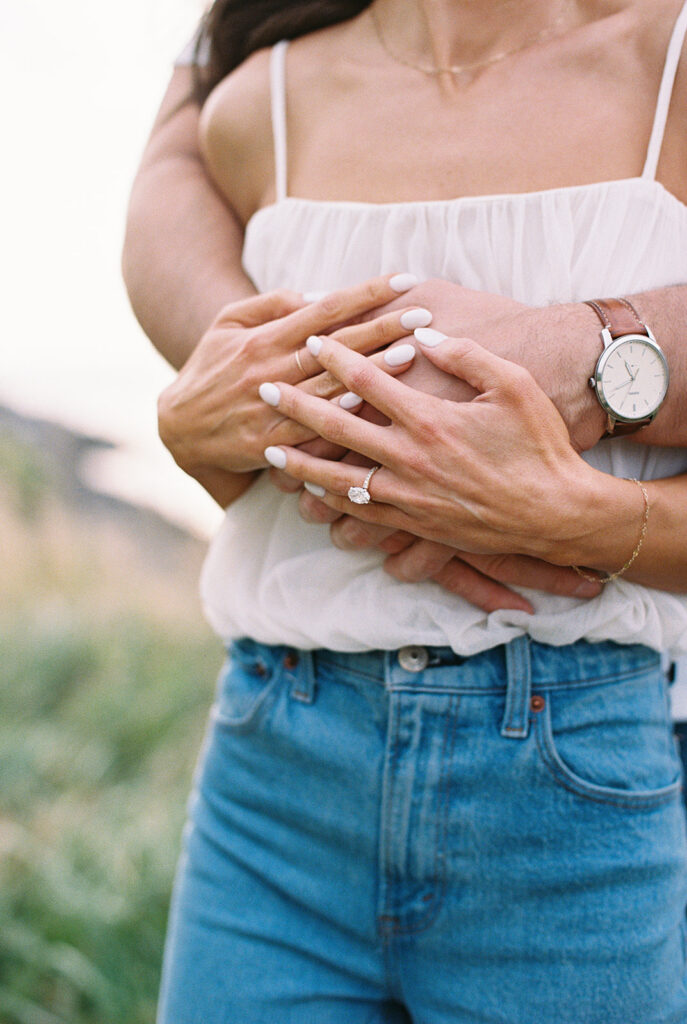 Engagement ring and watch detail as Zach wraps his arms around Carolyn on the Cape May beach