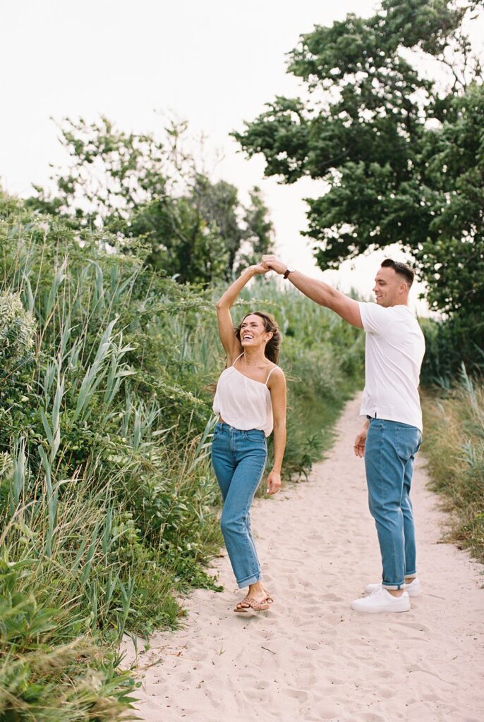 Carolyn and Zach dancing and twirling on a sandy beach path during their playful Cape May engagement session