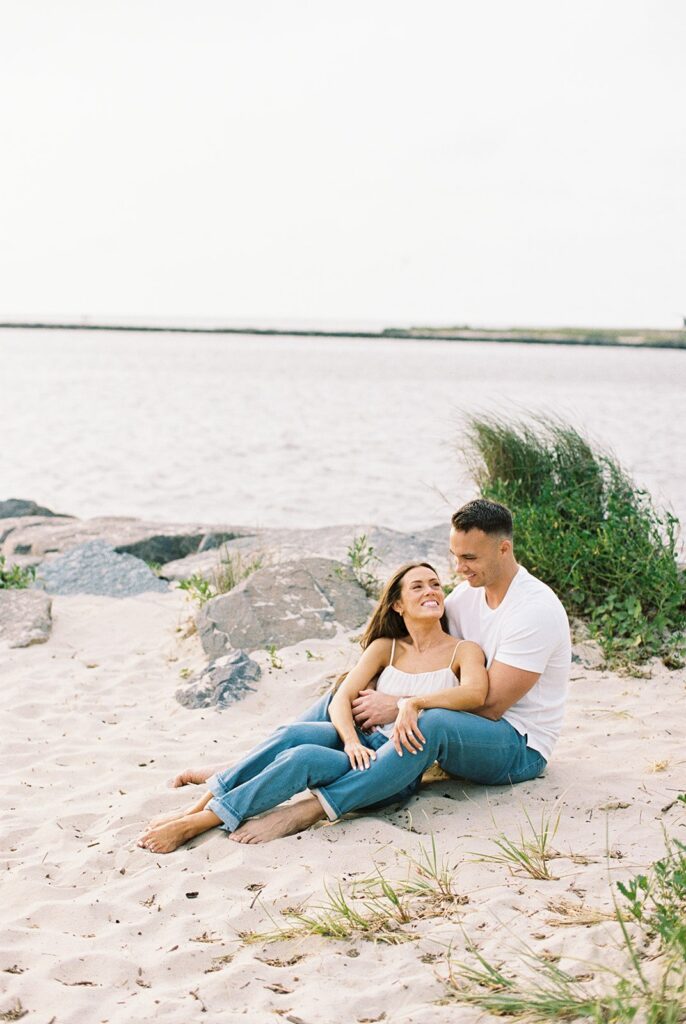 Engaged couple relaxing on the sand by the bay during their Cape May beach engagement session