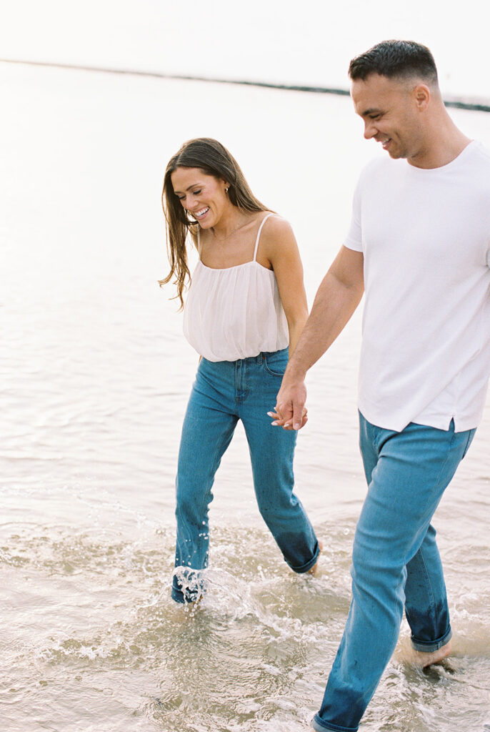 Engaged couple splashing through the shallows holding hands at their summer Cape May beach engagement session