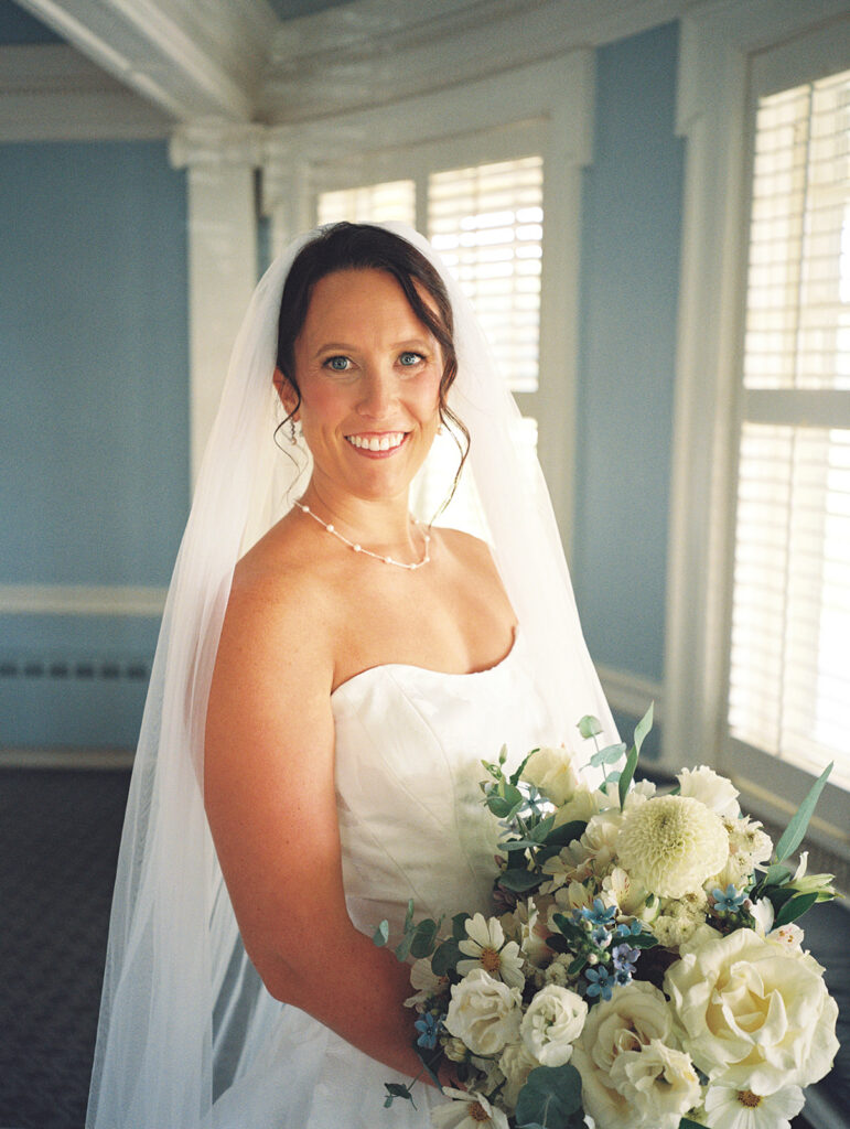 Film portrait of the bride in a strapless gown and veil holding a blue and white bouquet in a sunlit blue room, a blue and white Philadelphia Cricket Club wedding