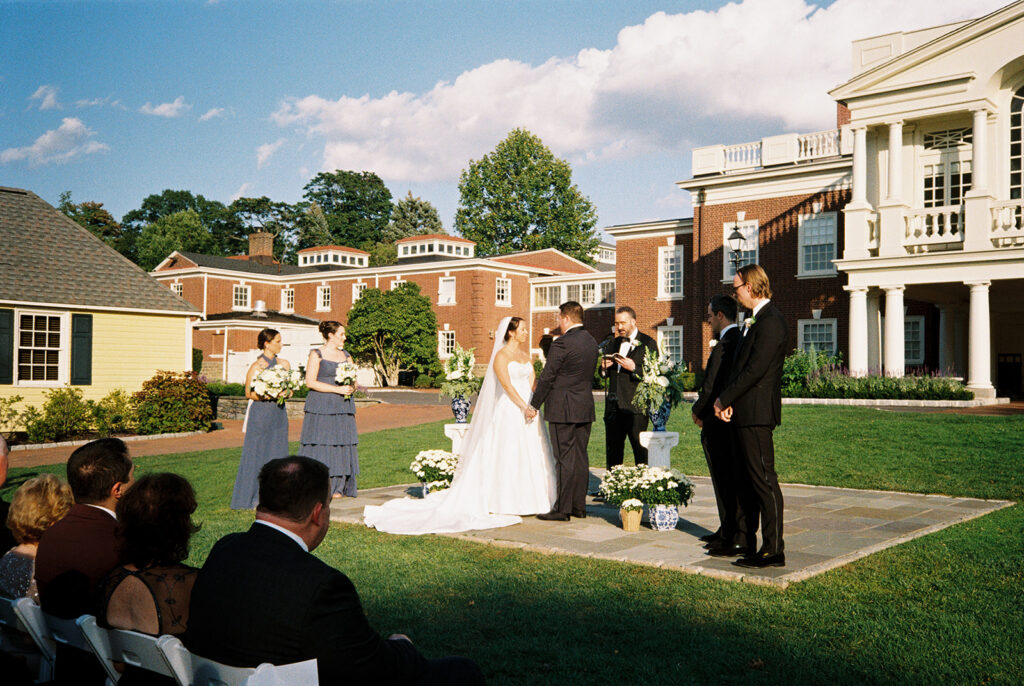 Outdoor lawn ceremony at the Philadelphia Cricket Club with blue and white china vases beside the couple and bridesmaids in dusty blue, on film