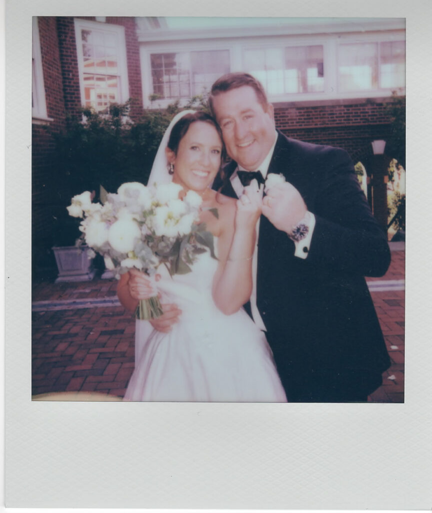 Polaroid close-up of the bride and groom laughing, the bride holding her white bouquet outside the brick clubhouse