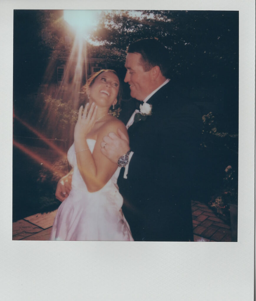 Polaroid of the bride and groom laughing together in golden light, sun flaring over the brick patio