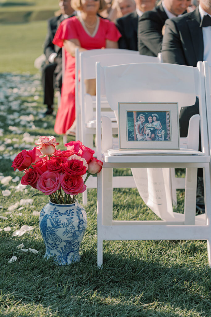 Blue and white china vase of pink roses beside a framed photo of the bride's late mother, Jeanne, on a reserved ceremony chair