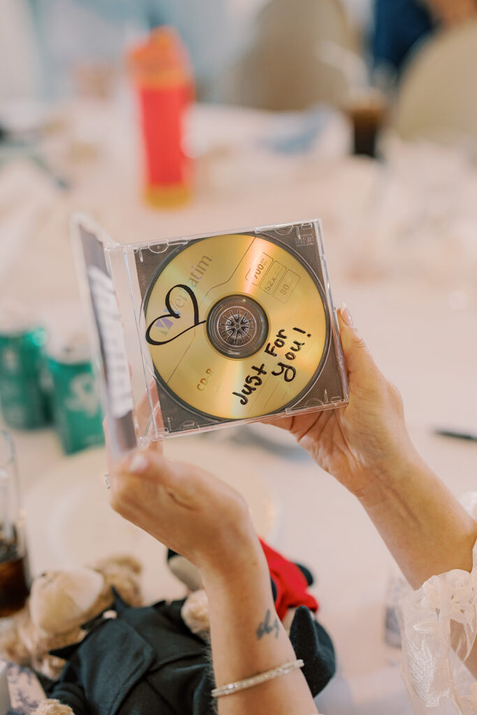 The bride holds up the "Just For You" mixtape CD her groom gave her, a heart drawn on the gold disc