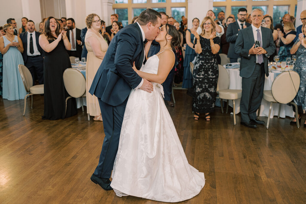 Bride and groom share their first dance as guests cheer around the wood dance floor at a blue and white Philadelphia Cricket Club wedding