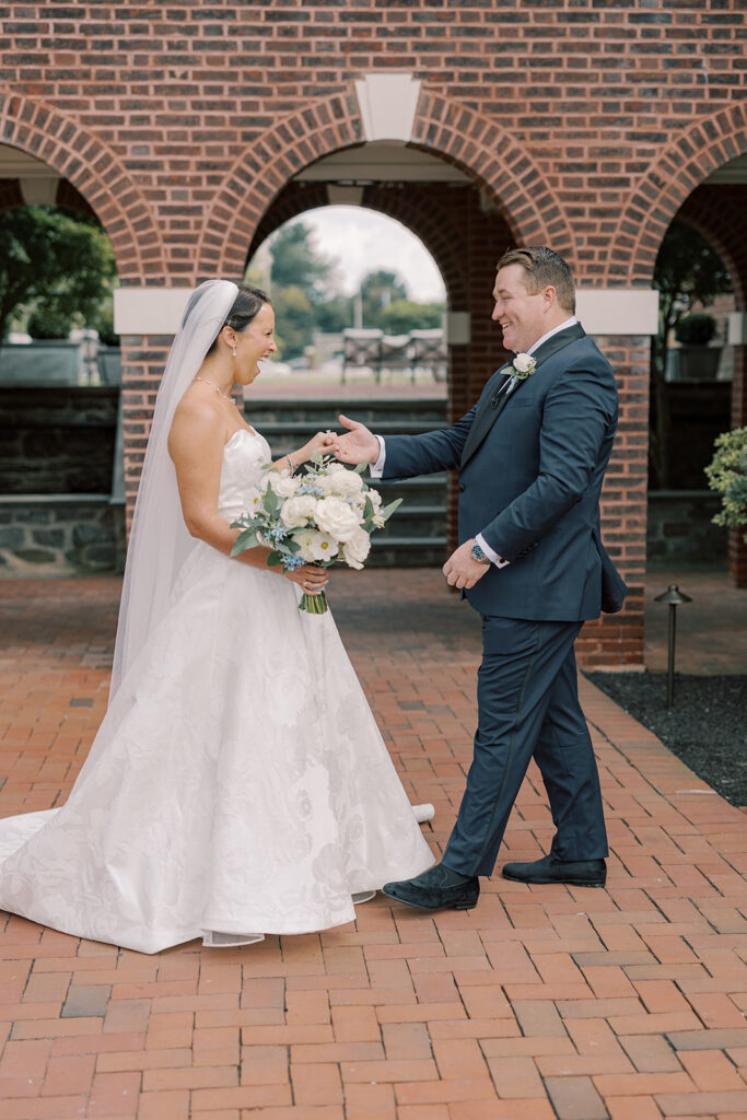 Bride and groom laugh during their first look at a blue and white Philadelphia Cricket Club wedding, beneath the brick archways