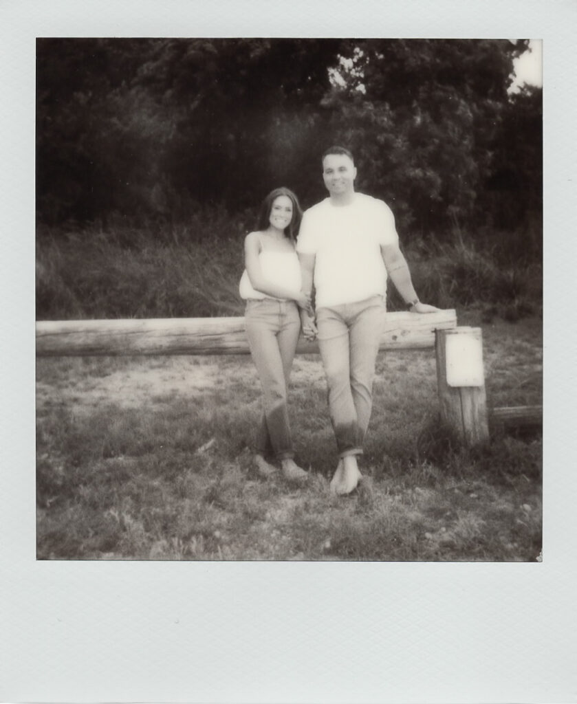Sepia Polaroid of Carolyn and Zach leaning against a wooden fence in a grassy field during their Cape May engagement session