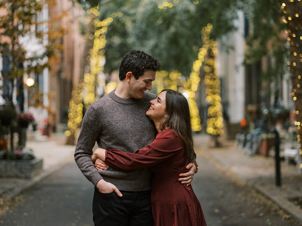 Amy and Chas pause in the residential backstreets near Rittenhouse Square with trees wrapped in glowing string lights in the background