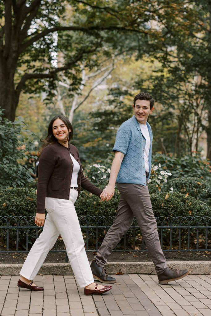 Amy and Chas walking hand in hand along a tree-lined path during their Rittenhouse Square engagement session