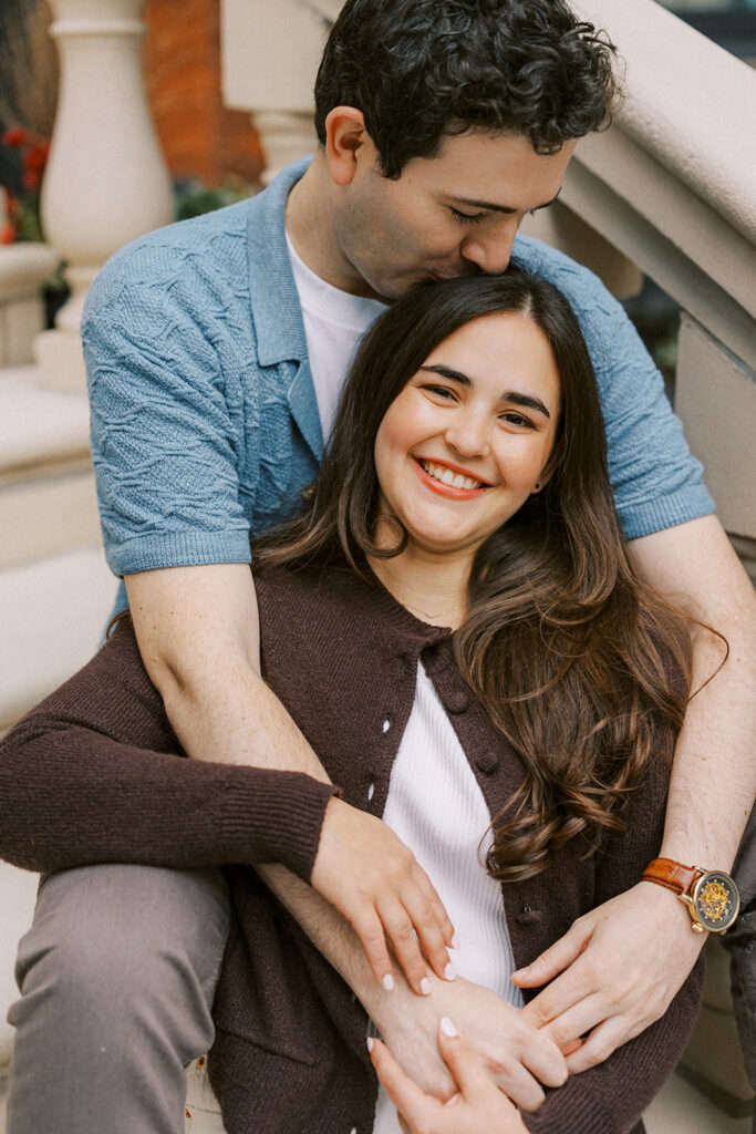 Engaged couple cuddles close together on the staircase outside a row of brownstones near Rittenhouse Square