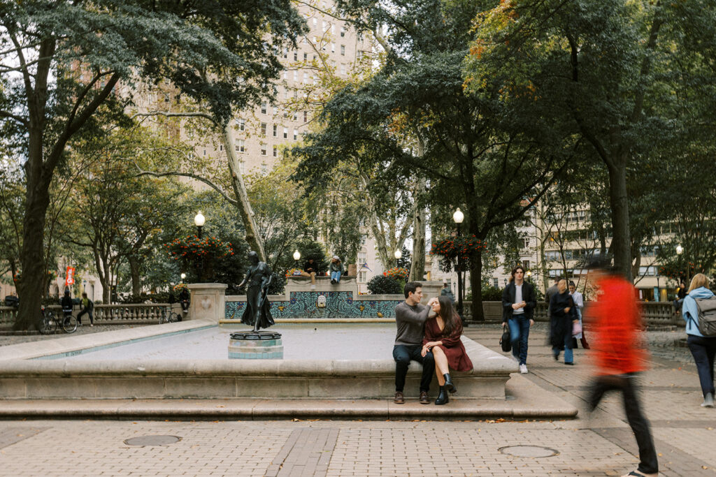 Couple sitting on the edge of the central fountain during a fall engagement session in Philadelphia at Rittenhouse Square